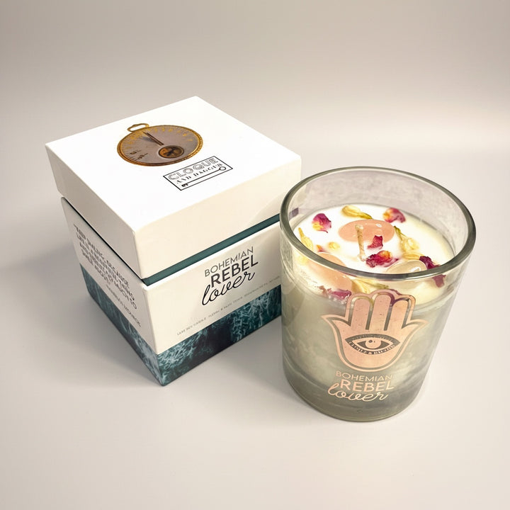 Cloque and Dagger Bohemian Rebel Lover candle in a glass vessel with Hamsa hand symbol, topped with rose petals and crystals.